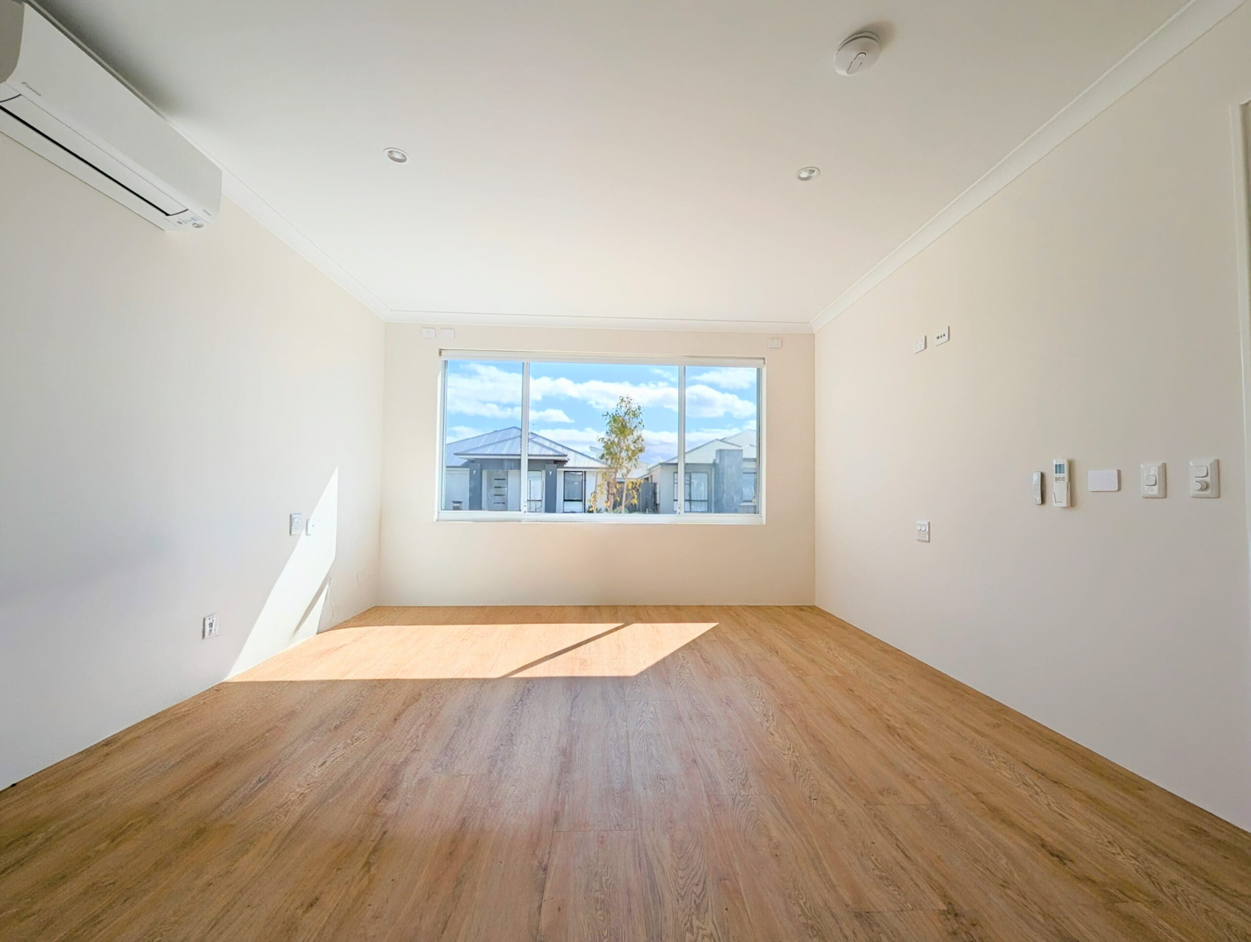Bright, accessible bedroom in an SDA Property in Baldivis, featuring wood-look flooring, large window, and wall-mounted air conditioning, part of Australia’s leading disability accommodation provider.