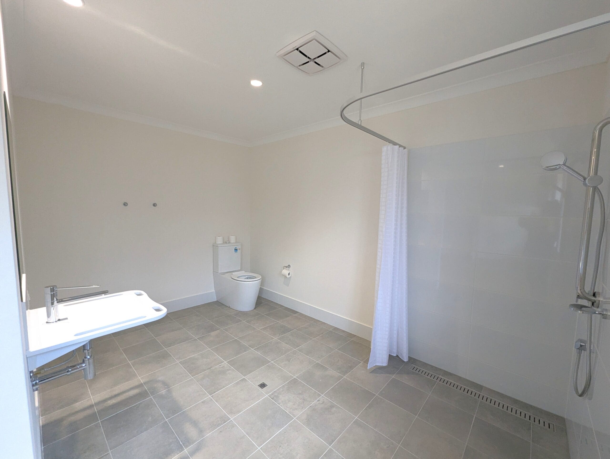 Accessible bathroom in an SDA Property in Baldivis, featuring walk-in shower, wall-mounted sink, and floor drain, part of Australia’s leading disability accommodation provider.