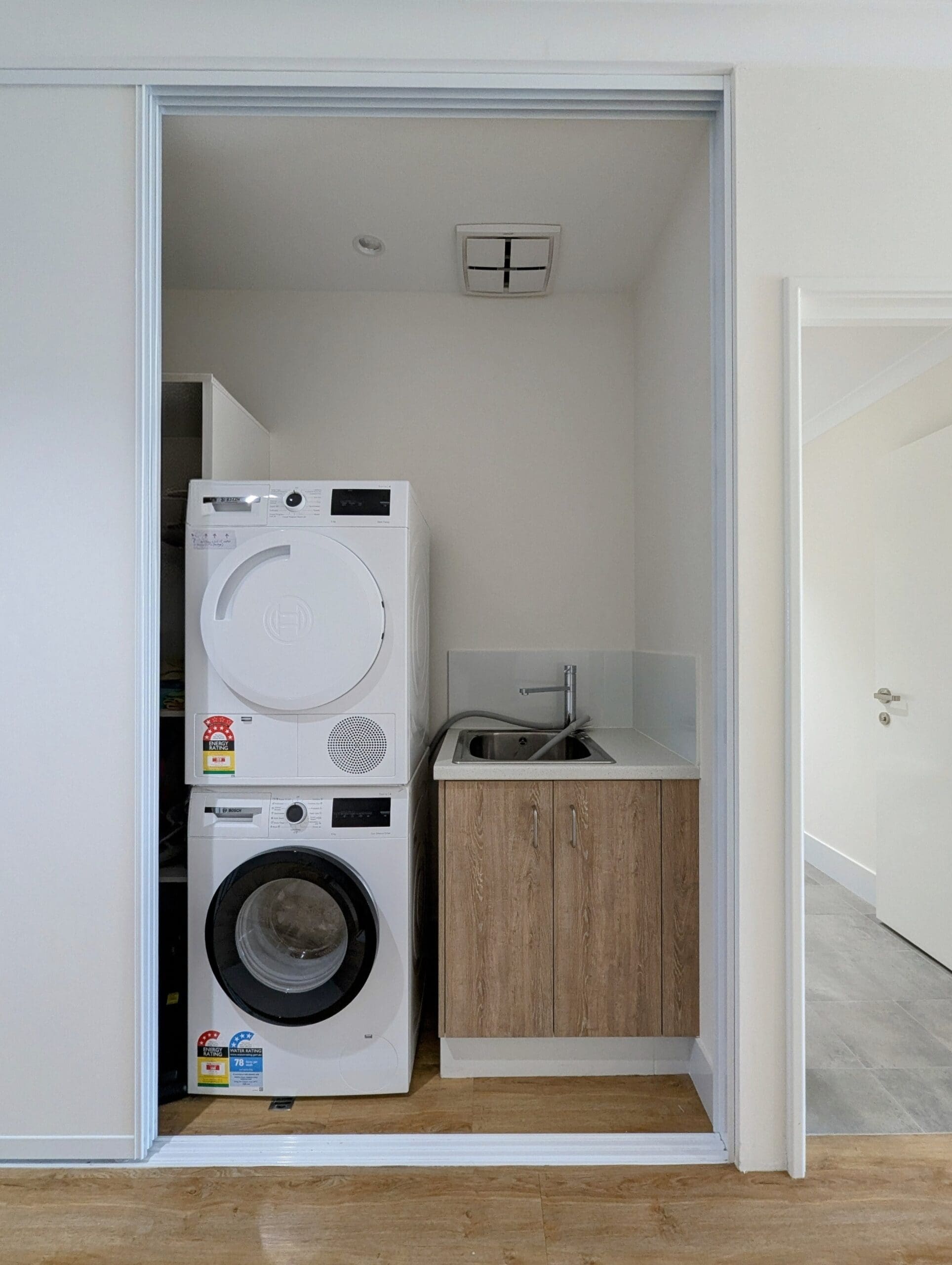 Laundry area in an SDA Property in Baldivis, featuring a stacked washer and dryer alongside a compact sink unit, part of Australia’s leading disability accommodation provider.