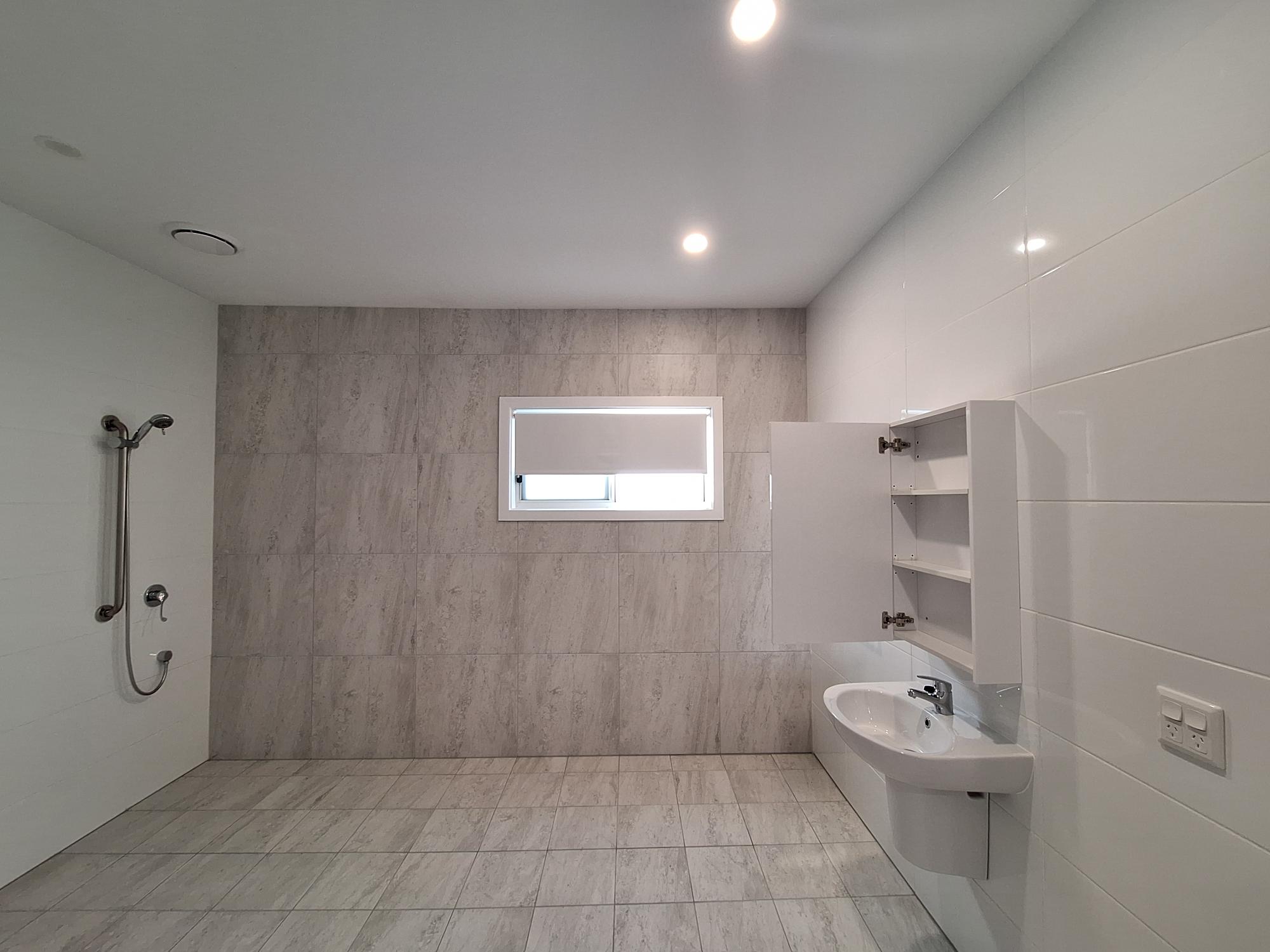 Accessible bathroom in a SIL in Brand New HPS Villas in Brassall, 14 Hayes St, Brassall Qld 4305, featuring walk-in shower, marble-effect tiles, and wall-mounted sink with storage, part of Australia’s leading disability accommodation provider.