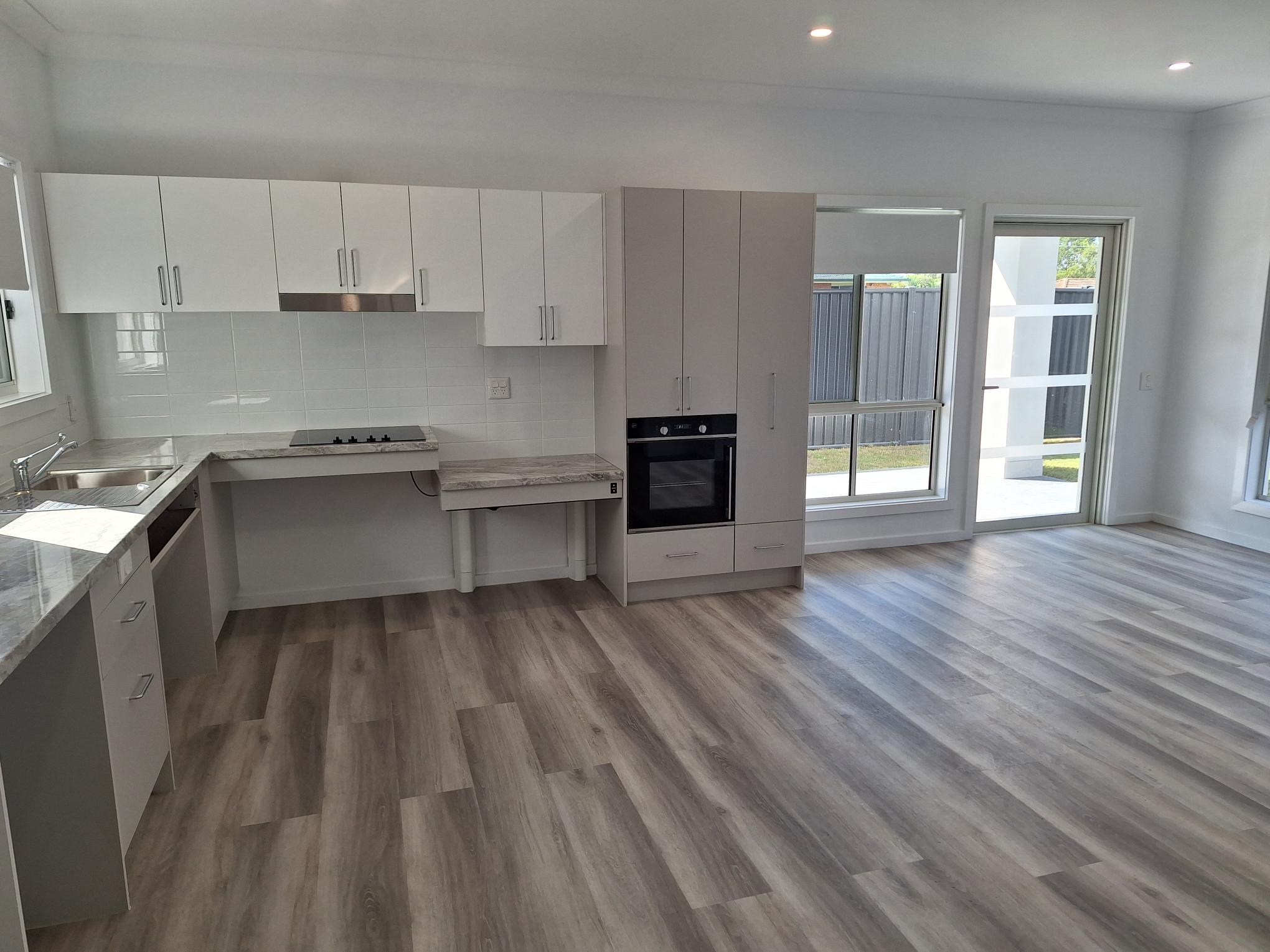 Spacious, accessible open-plan kitchen in a SIL in Brand New HPS Villas in Brassall, 14 Hayes St, Brassall Qld 4305, featuring light wood flooring, modern cabinets, and seamless indoor-outdoor access, part of Australia’s leading disability accommodation provider.