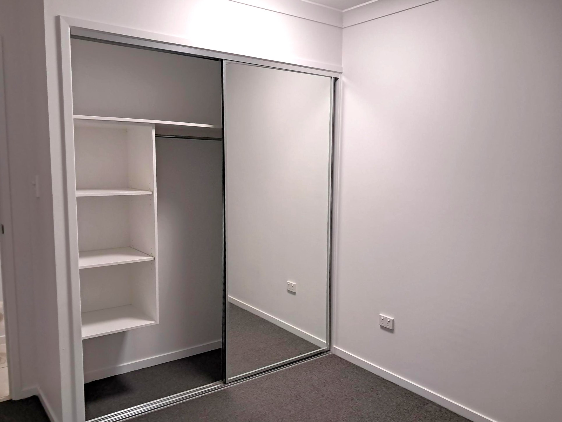 Built-in wardrobe with sliding mirrored doors and open shelving, part of a modern and accessible bedroom interior, from Australia's leading disability support provider.