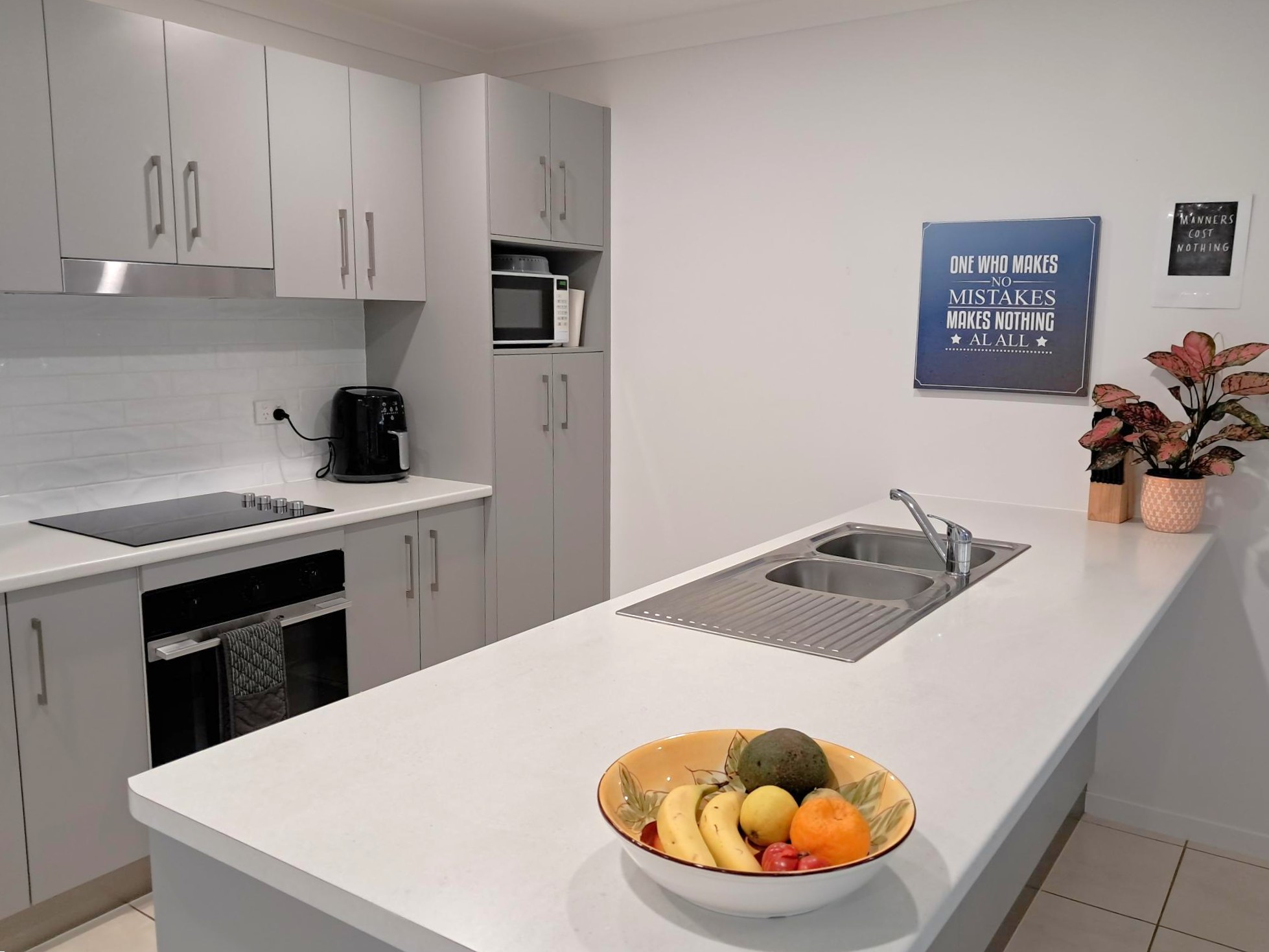Modern kitchen interior featuring grey cabinetry, electric cooktop, microwave, and island bench with sink and fruit bowl, from Australia's leading disability support provider.