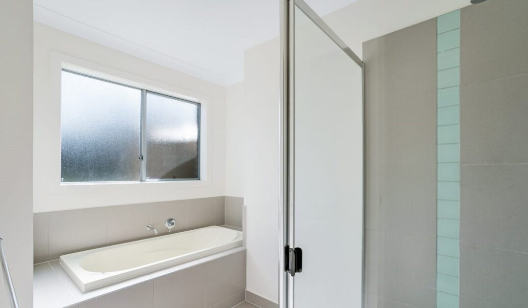 Modern accessible bathroom with glass shower, white vanity, and light blue tiled splashback, from Australia's leading care accommodation provider.