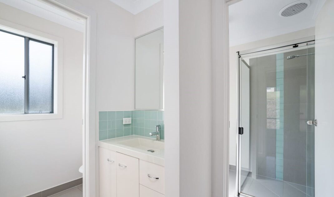 Modern accessible bathroom with glass shower, white vanity, and light blue tiled splashback, from Australia's leading care accommodation provider.