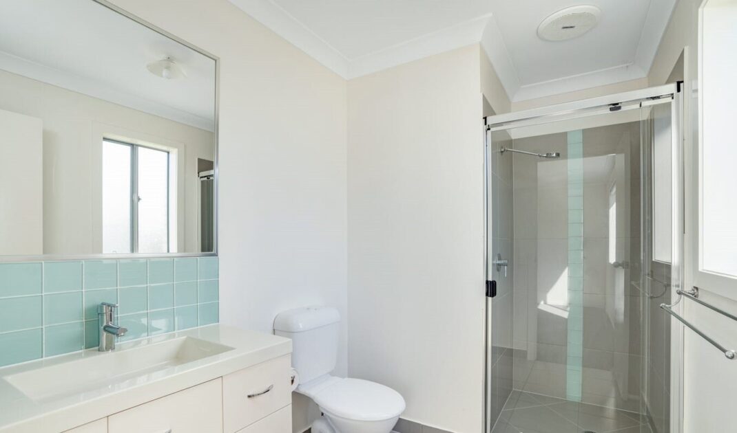 Modern accessible bathroom with glass shower, white vanity, and light blue tiled splashback, from Australia's leading care accommodation provider.