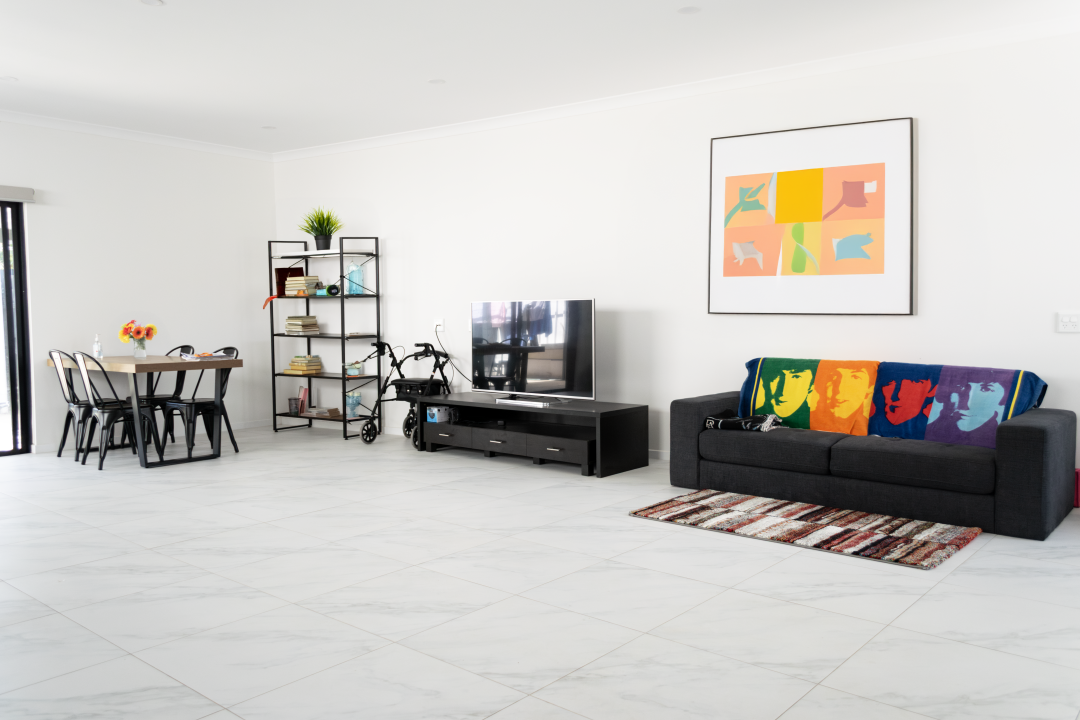 Spacious, accessible living area in a Beautiful Brand New SDA Home in Christie Beach, featuring marble-effect tiles, open-plan design, and modern furnishings, part of Australia’s leading disability accommodation provider.