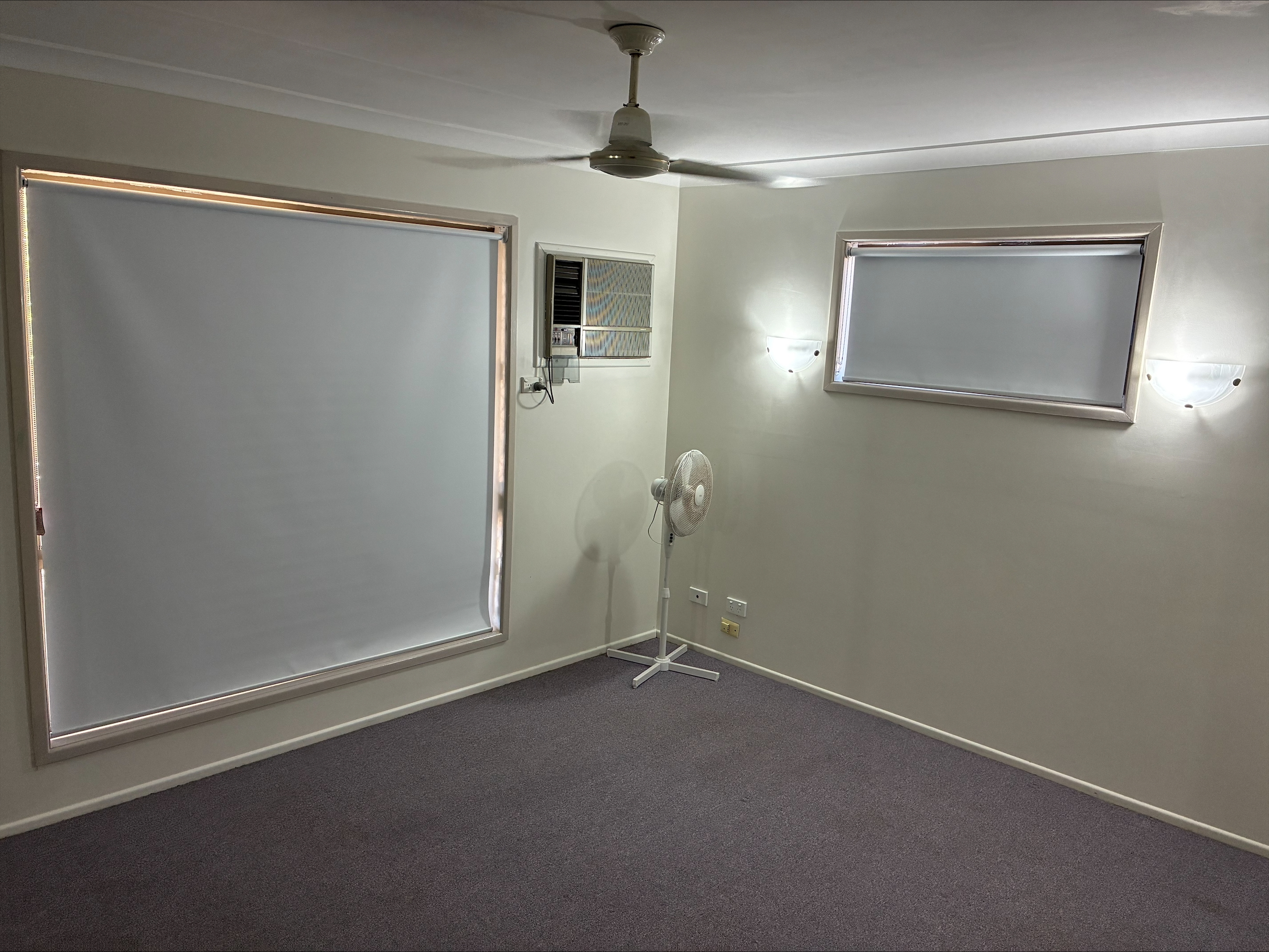 Calm, accessible bedroom in a Spacious SIL Home in the Heart of Rockhampton, 23 O'Shanesy Street, Koongal Qld 4701, featuring grey carpet, large windows, and ceiling fan, part of Australia’s leading disability accommodation provider.