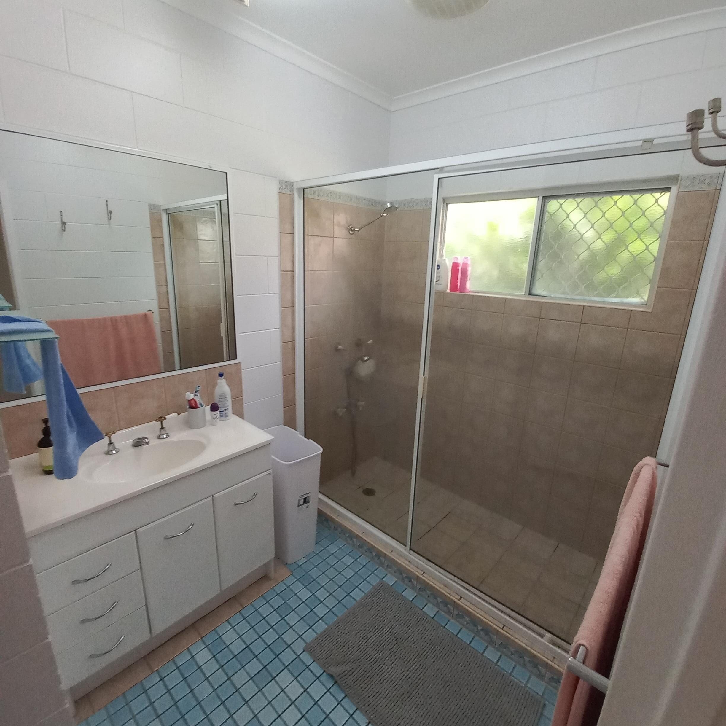 Accessible bathroom in a Spacious and Airy SIL home south of Cairns, featuring walk-in shower, blue mosaic tiles, and wall-mounted sink, part of Australia’s leading disability accommodation provider.