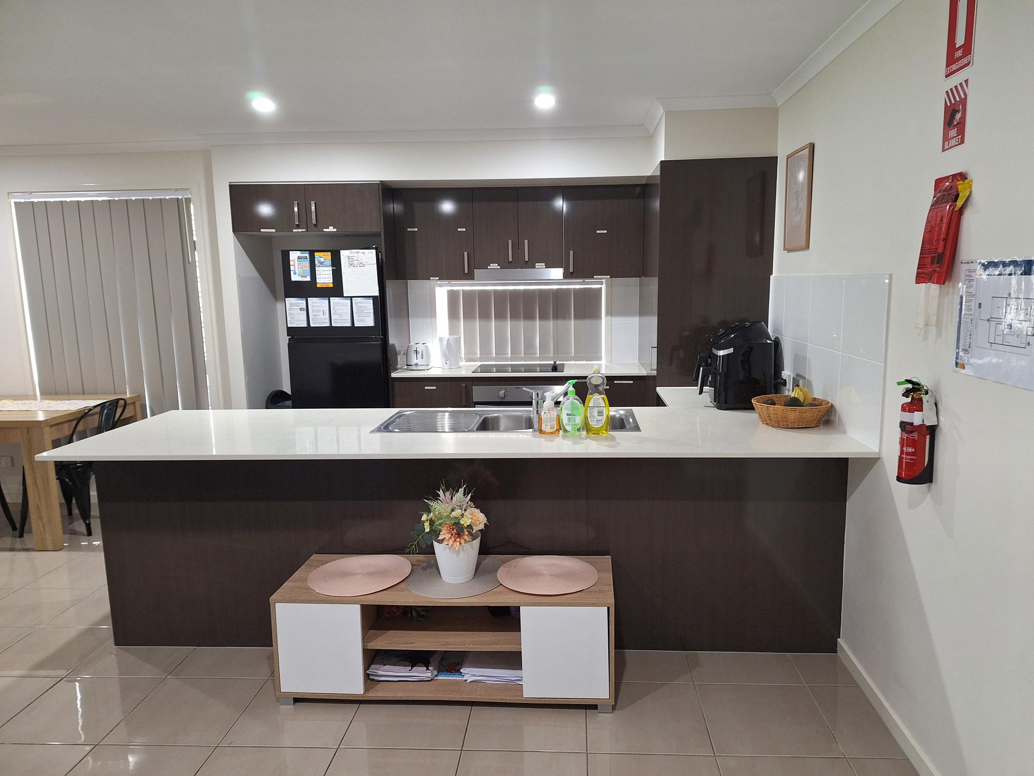 Accessible, modern kitchen in Comfort of SIL in Tranquil Thornlands, featuring central island, dark cabinetry, and safety features, part of Australia’s leading disability accommodation provider.